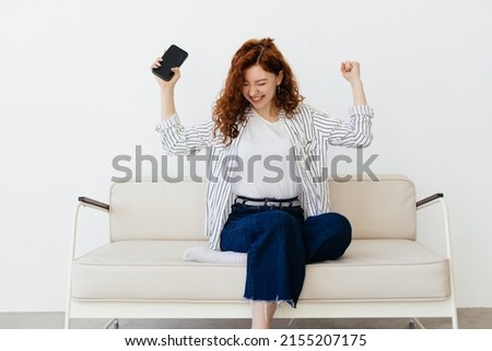Yes. Portrait of lucky woman holding and using her cell phone, shaking fist, screaming yeah, celebrating win or victory, playing games online, reading great news, sitting on couch
