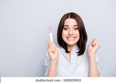 Yes, I am pregnant! Portrait of attractive charming pretty brunette surprised glad woman demonstrating positive result on pink and white test stick isolated on grey background