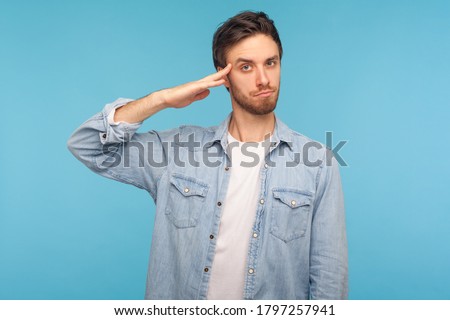 Yes sir! Portrait of responsible patriotic man in worker denim shirt saluting with respect as if soldier waiting order from commander, obeying discipline. studio shot isolated on blue background
