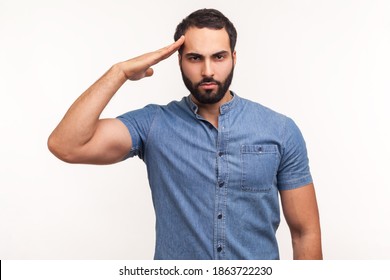 Yes sir! Subordinate disciplined man with beard saluting, holding hand near head, looking at camera with serious expression, patriotism and discipline. Indoor studio shot isolated on white background - Shutterstock ID 1863722230