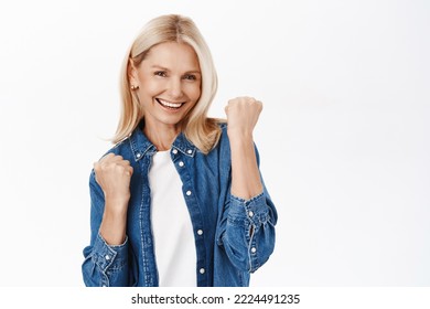 Yes, Success. Excited Blond Mature Woman Celebrating, Makes Fist Pump And Smiles Satisfied, Achieve Goal, Triumphs, Stands Over White Background.