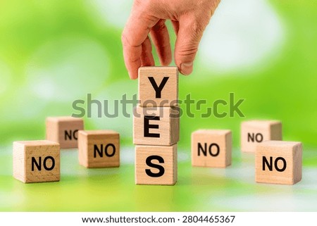 Yes vs No with a hand stacking wooden blocks to spell Yes among surrounding No voices as a motivational business concept of fearlessness and conviction to one's own decisions despite bad advisors. Copy space