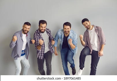 Yes We Did It, We're Winners. Group Of 4 Cheerful Friends Celebrating Victory Or Having Fun At Party. Happy Handsome Caucasian Men In Shirts And Jeans Fist Pumping In Studio With Light Gray Background