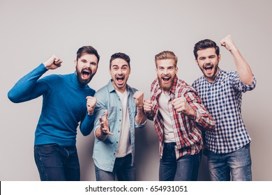 Yes! Winners! Four cheerful young men are standing and gesturing for the victory on pure background in casual outfit and jeans. They are fans of sports games as football, basketball, hockey, baseball