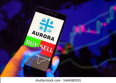 YESSENTUKI, RUSSIA - July 27, 2019: Company logo Aurora Cannabis Inc. (ACB) on smartphone screen, hand of trader holding mobile phone showing BUY or SELL on background of stock chart