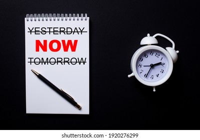 YESTERDAY NOW TOMORROW is written in a white notepad near a white alarm clock on a black background.