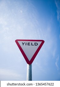 Yield road sign with blue sky and the word yield printed on it before a roundabout, Ireland.