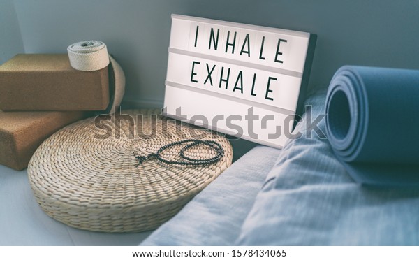 Yoga\
breathing INHALE EXHALE sign at fitness class on lightbox\
inspirational message with exercise mat, mala beads, meditation\
pillow. Accessories for fit home\
lifestyle.