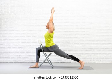 Yoga with a chair. Fit caucasian woman practice warrior pose using props in loft white studio indoor.