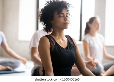 Yoga class concept, close up focus on mixed race African female closed eyes do meditation practice with associates during session. No stress, reducing fatigue after work out sport activity, wellness