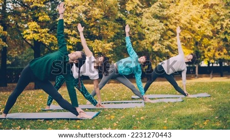 Yoga class is doing stretching exercises in park enjoying autumn nature, fresh air and physical activity. Well-being, recreation and sporty young people concept.