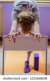 Yoga Class, Downward Facing Dog With The Help Of A Chair Done By Female Practitioner.