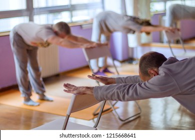 Yoga class, downward facing dog with the help of a chair done by three practitioners.