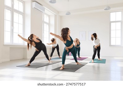 Yoga class group in studio practicing pose. Women on mats stretching into triangle, focusing alignment. Bright interior supports mindful fitness and balance. Group wellness and balance concept. - Powered by Shutterstock - Get 15% off with code: PIKWIZARD15