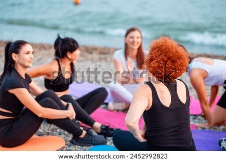 Yoga class. Group of young-adult multi-racial women are sitting on sports mats on wild beach and talking to each other. Concept of female circle of communication and support.