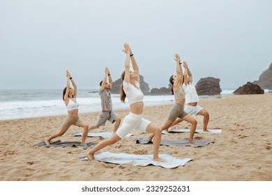 Yoga class on ocean shore. Group of young people doing warrior pose, meditating and exercising on the beach. Wellness and healthy balance lifestyle - Powered by Shutterstock