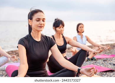 Yoga class at sea coast. Group of Caucasian women meditating on sports mats at pebble beach. Outdoor training and wellness. - Powered by Shutterstock