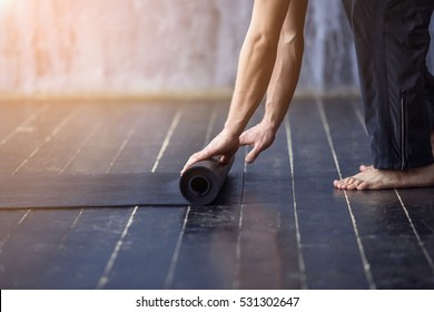 Yoga Concept. Young Yogi Men Rolling Mat After A Yoga On Black Wooden Floor