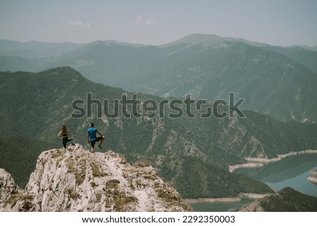 Yoga couple doing yoga pose with leg up at the top of the mountain