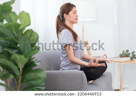 Yoga exercise concept, Young Asian woman doing yoga exercise in lotus pose on couch in living room.