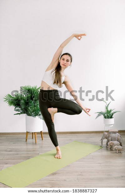 Yoga and fitness\
concept, Vrksasana or tree pose. Front view of slim pretty girl,\
doing yoga tree pose, gesturing mudra, standing in modern light\
studio, full length