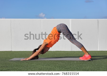 Yoga fitness woman stretching doing morning practice on exercise mat at outdoor park. Girl doing leg stretch with downward facing dog beginner's class.