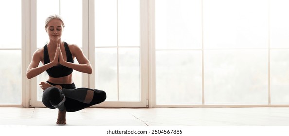 Yoga girl balancing on one leg, placing hands in namaste, perfoming advanced yoga pose in fitness studio, empty space - Powered by Shutterstock