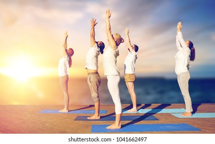 concepto de yoga y estilo de vida saludable - grupo de personas haciendo saludos al alza posan en un muelle de madera sobre el fondo del mar