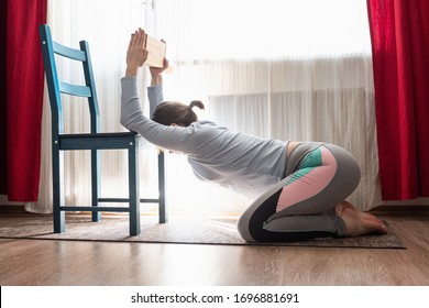 Yoga at home. Woman stretching and opening shoulders using chair at the living room.