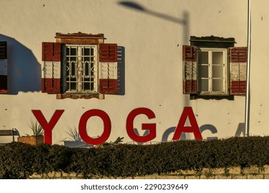 A yoga house in the village of Poertschach at the Woerthersee in Carinthia, Austria. The sun is hitting the walls of the house. The window blinders are open. Big yoga sign in front of the building
