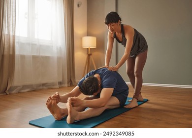 Yoga instructor assisting student in forward bend pose during home practice - Powered by Shutterstock