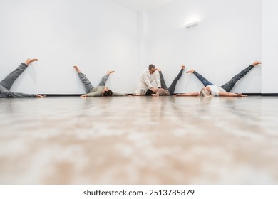 A yoga instructor assists a group of senior women performing the legs-up-the-wall pose during a yoga session. Concept of guided senior yoga for health and relaxation. - Powered by Shutterstock