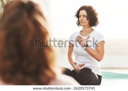 Yoga instructor doing breathing exercise with her class in a yoga studio. Mature woman leading a holistic workout at a health club. Finding balance and peace with meditation for a healthy lifestyle