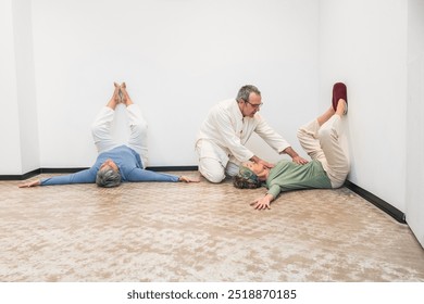 A yoga instructor guides senior women in a restorative yoga session with legs up the wall. Concept of assisted yoga practice for relaxation and well-being. - Powered by Shutterstock