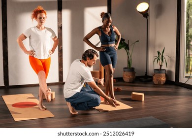 A yoga instructor guides two women in a yoga studio. The women are performing yoga poses while the instructor assists them. The studio has large windows and a calm atmosphere. - Powered by Shutterstock