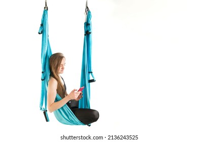 Yoga Instructor Has Break And Holding Phone. Young Athletic Woman Hang In Hammock During An Aerial Gymnastics Or Fly Yoga Workout