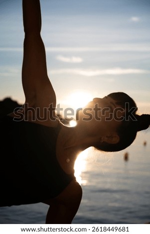 Yoga instructor practicing a side plank variation at sunset on the beach