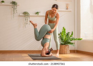 Yoga instructor training with Asian women wearing green sportswear.Healthy Female Working out against wooden floor, doing yoga workout exercise. Handstand,headstand.Private yoga training at home - Powered by Shutterstock