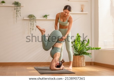 Yoga instructor training with Asian women wearing green sportswear.Healthy Female Working out against wooden floor, doing yoga workout exercise. Handstand,headstand.Private yoga training at home