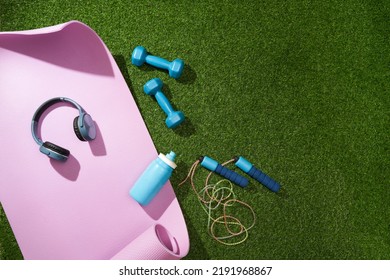 Yoga Mat With Dumbbells, Jump Rope, Headphones And Water Bottle On Green Grass. Sport Gear.