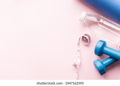 Yoga Mat, Dunbbells, Measuring Type And Water Bottle On Pink Background. Weight Loss, Fitness, Sport Concept. Top View. Copy Space.