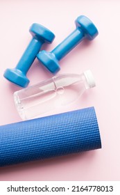 Yoga mat, dunbbells and water bottle on pink background. Weight loss, fitness, sport concept. Top view.