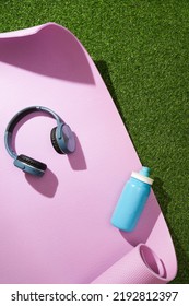 Yoga Mat With Headphones And Water Bottle On Green Grass. Sport Gear.