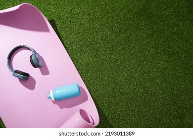 Yoga Mat With Headphones And Water Bottle On Green Grass. Sport Gear.