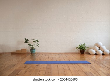 Yoga mat lying on wood floor in a yoga studio. Yoga studio decorated with sport's equipment and tropical plants.