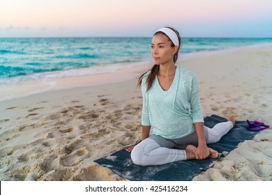 Yoga Mat Woman Stretching Hip, Hamstring Muscles And Groin Area, Leg Muscles With Pigeon Pose Stretch. Fit Asian Fitness Athlete Girl Exercising Sports Stretches In Activewear On Beach At Sunset.