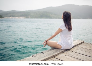 Yoga and meditation concept.Woman meditating in sitting yoga position on pier.Woman alone practicing mindfulness meditation to clear her mind.Zen,meditation,peace concept