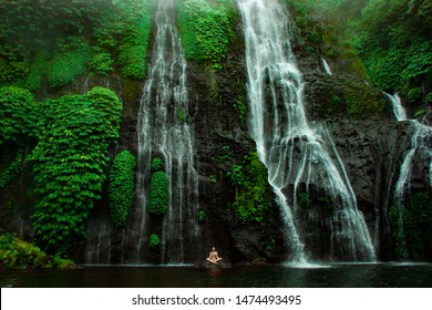 Yoga meditation on green tropical waterfall on Bali. Huge powerful water with small person under. Open chakra heal meditate concept 