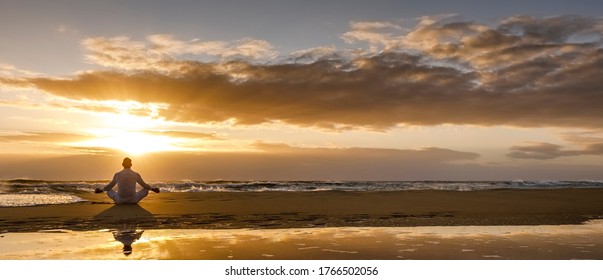 yoga meditation silhouette lotus sunrise beach, mindfulness, wellness and wellbeing concept, water reflection of man in yoga lotus pose sitting alone on sand with ocean cloud background, copy space - Shutterstock ID 1766502056