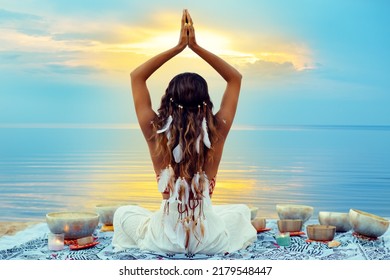 Yoga Meditation At Sunset Beach. Peaceful Woman Relaxing With Tibetan Singing Bowls. Indian Women Silhouette Meditating Over Sunshine Blue Sky Background